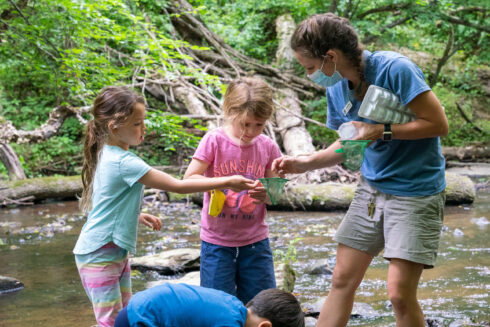 Two young campers are showing a Park Naturalist what they caught in their green dip net.