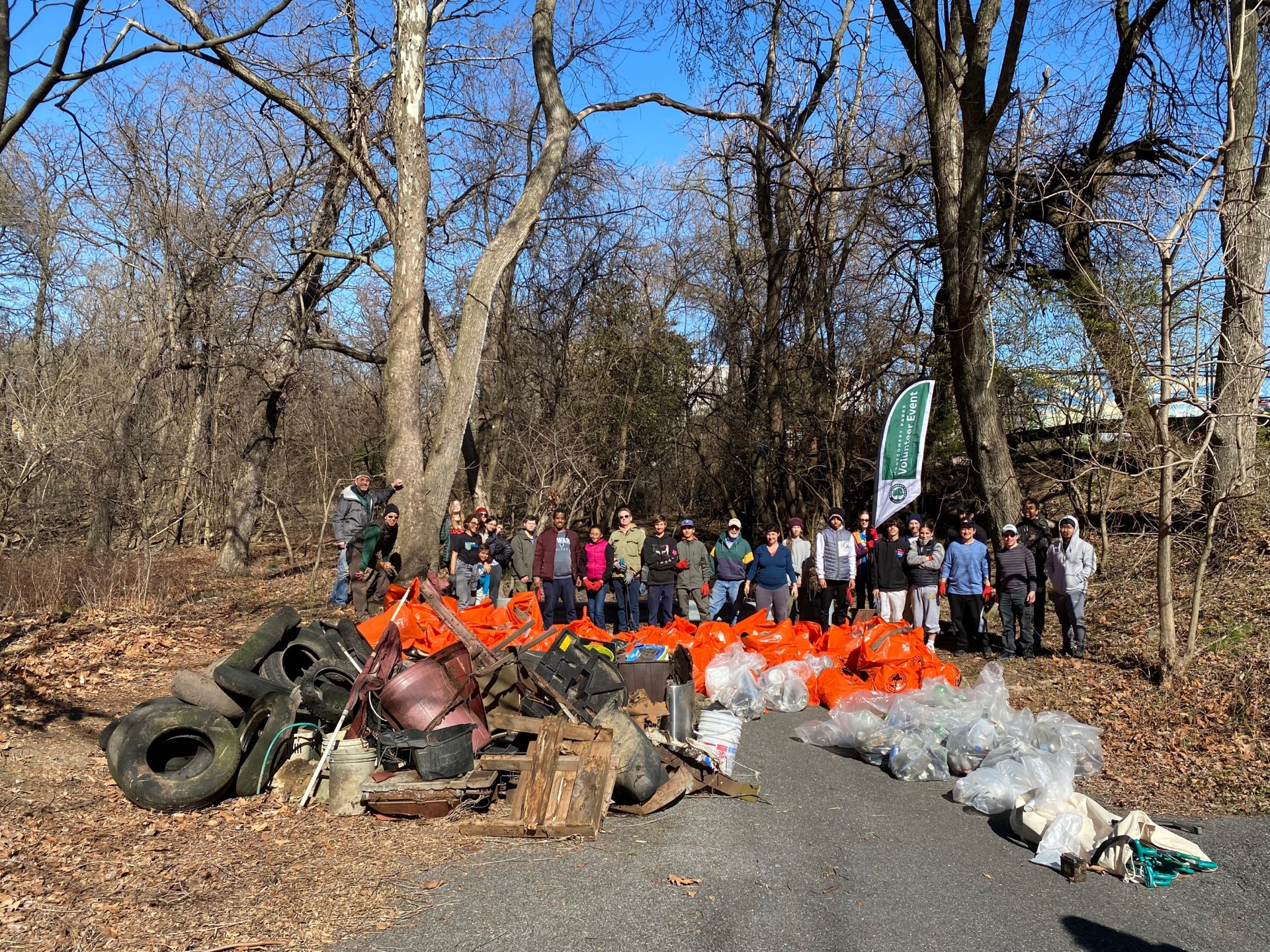 Volunteer group at a park standing in front of over 30 trash bags and tires.