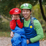 Dad dressed as Luigi holding daughter on knee who is dressed as Mario