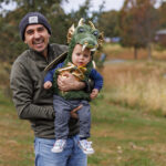 Father proudly holding up his son who is dressed in a green and gold dinosaur costume