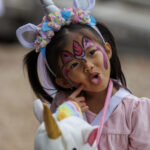 Little girl dressed as a unicorn posing for picture with pointer finger to cheek and tongue sticking out