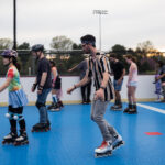Close up of people skating on rink with a girl on the left in a tie dye shirt and a man in his 20's wearing a striped shirt