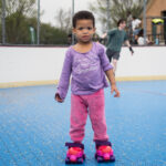 Little girl dressed in purple and pink wearing plastic training rollerskates