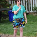 full body pic of stacey performing stand up with a wired mic in hand on a patio in colorful patterned shorts and an aqua t shirt