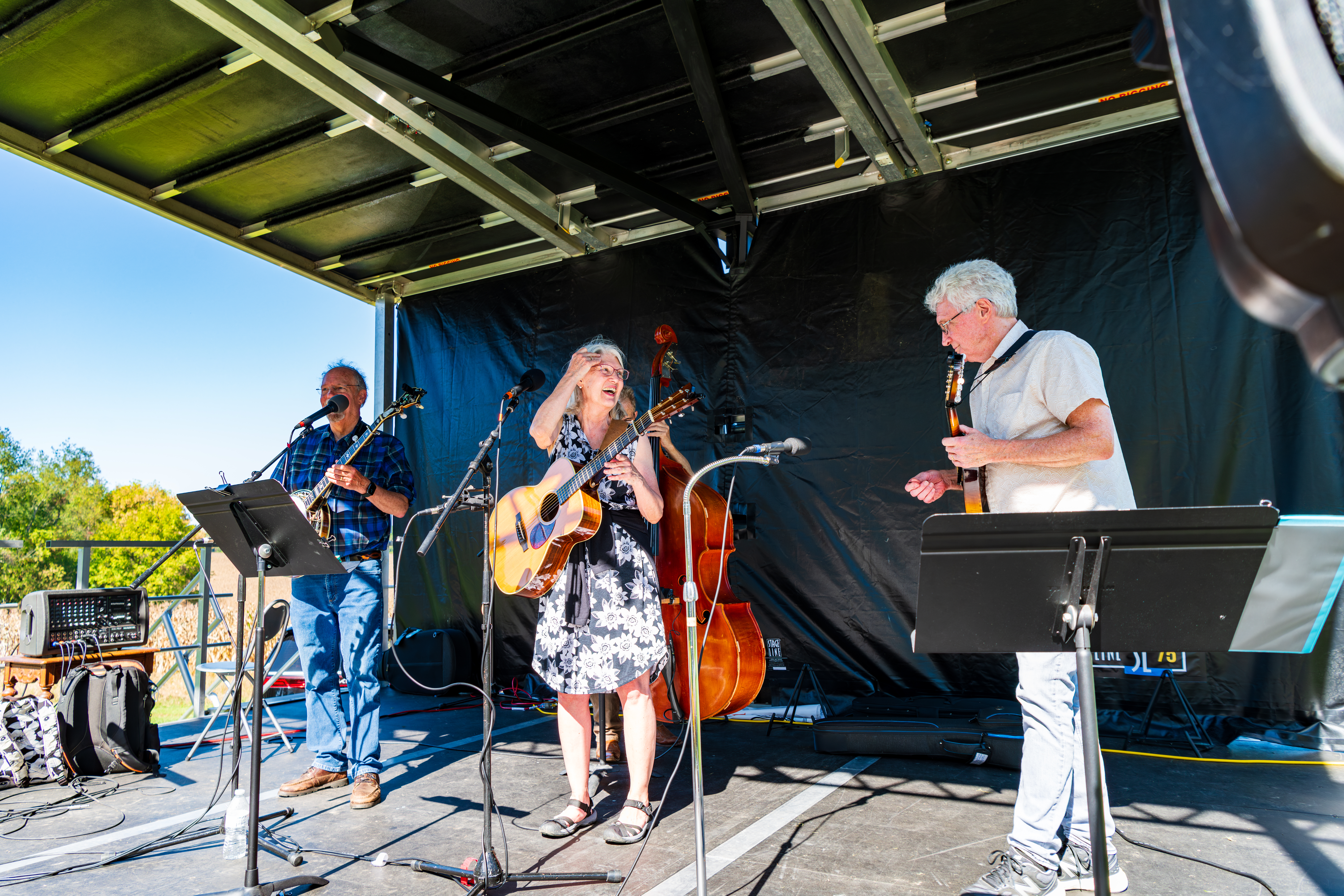 A band consisting of three people on a small outdoor stage wit instruments 