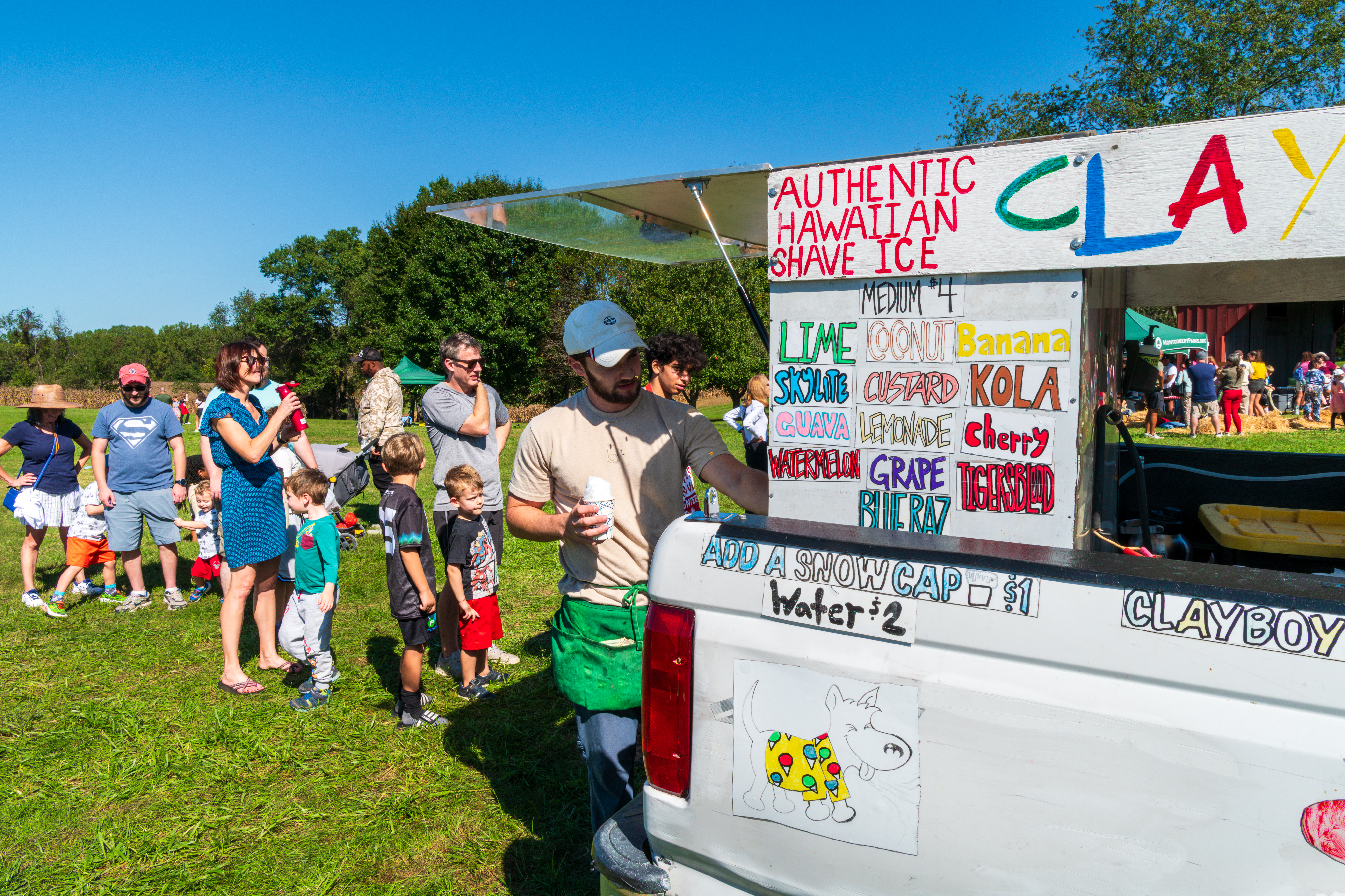 People standing in line behind a man scoping shaved ice out of a freezer on a pick up truck 