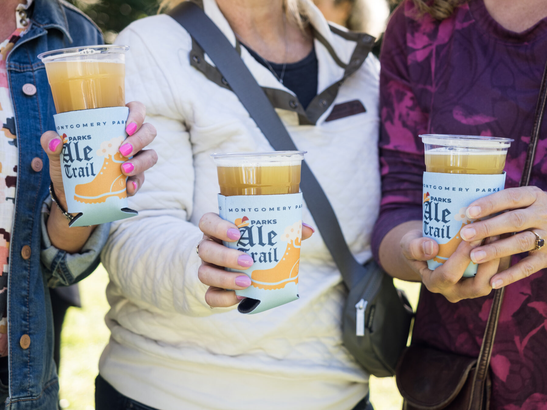 Upclose three people holding beer-filled plastic cups with Parks Ale Trail branded cozy.