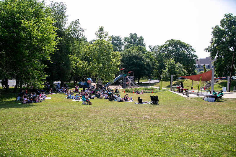 A crowd of people sit on the grass at Ellsworth Urban Park