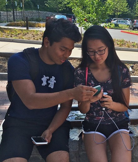 Two teens sitting on a park bench looking at a smartphone together.