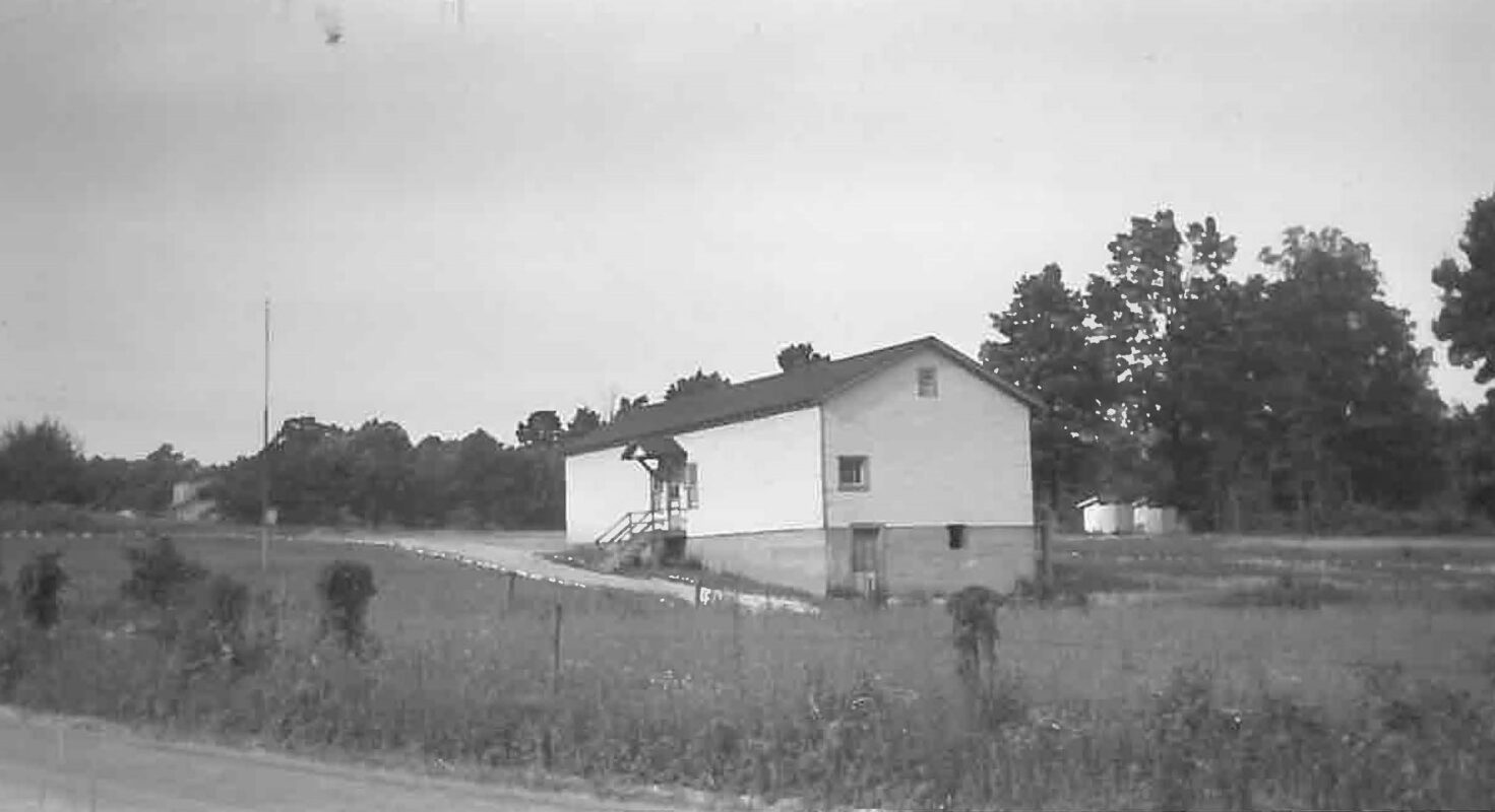 A black and white photo of a two-room schoolhouse. White sides and dark, peaked roof.
