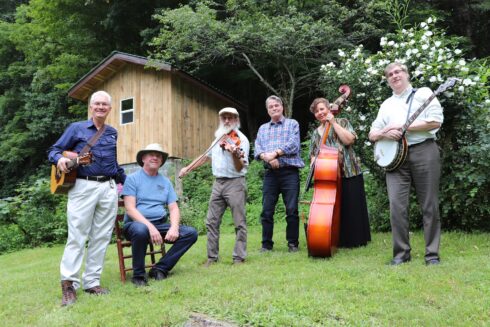 king street bluegrass band members posing with instruments on grassy hill with barn structure in background