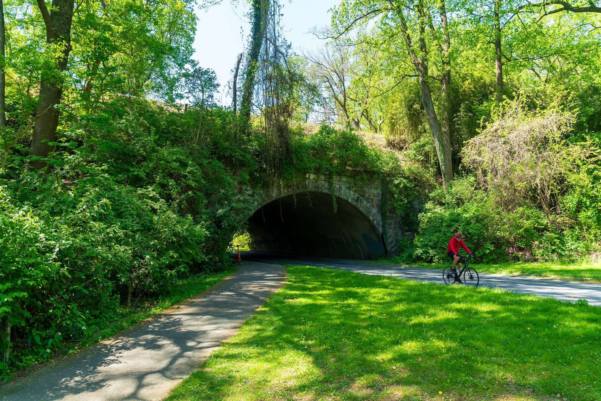Biker on trail with stone bridge tunnel in the background at Ken-Gar Palisades Local Park