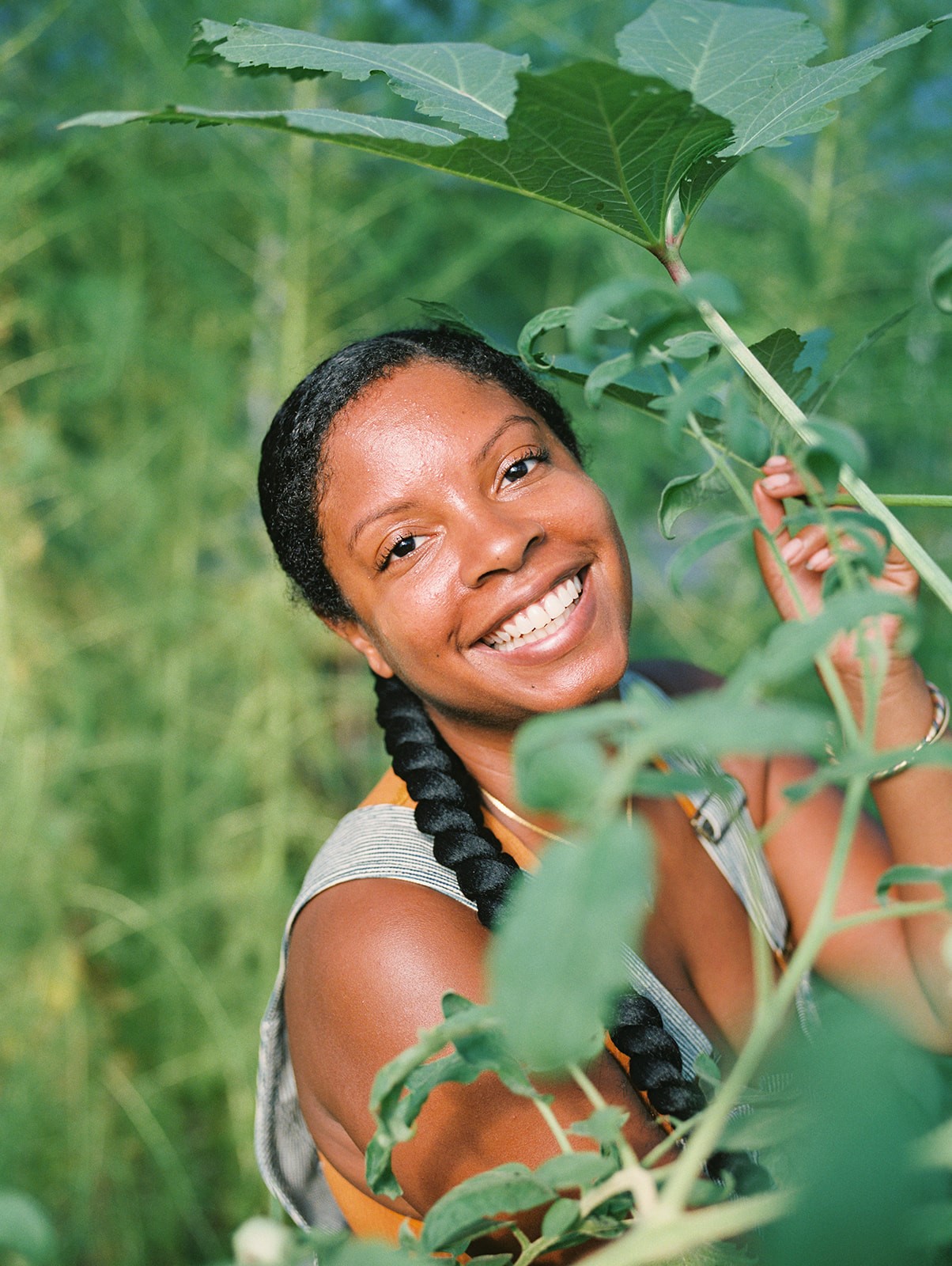 Falani Spivey smiles while standing next to okra plants.