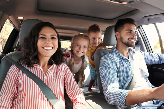 2 adults in front seat of car with 2 children in back smiling toward the dash for a picture