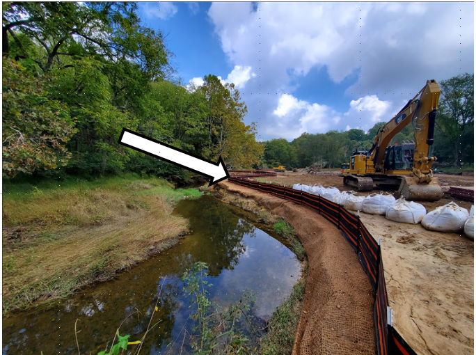 An active construction site, with a white arrow pointing to the erosion and sediment control fencing.