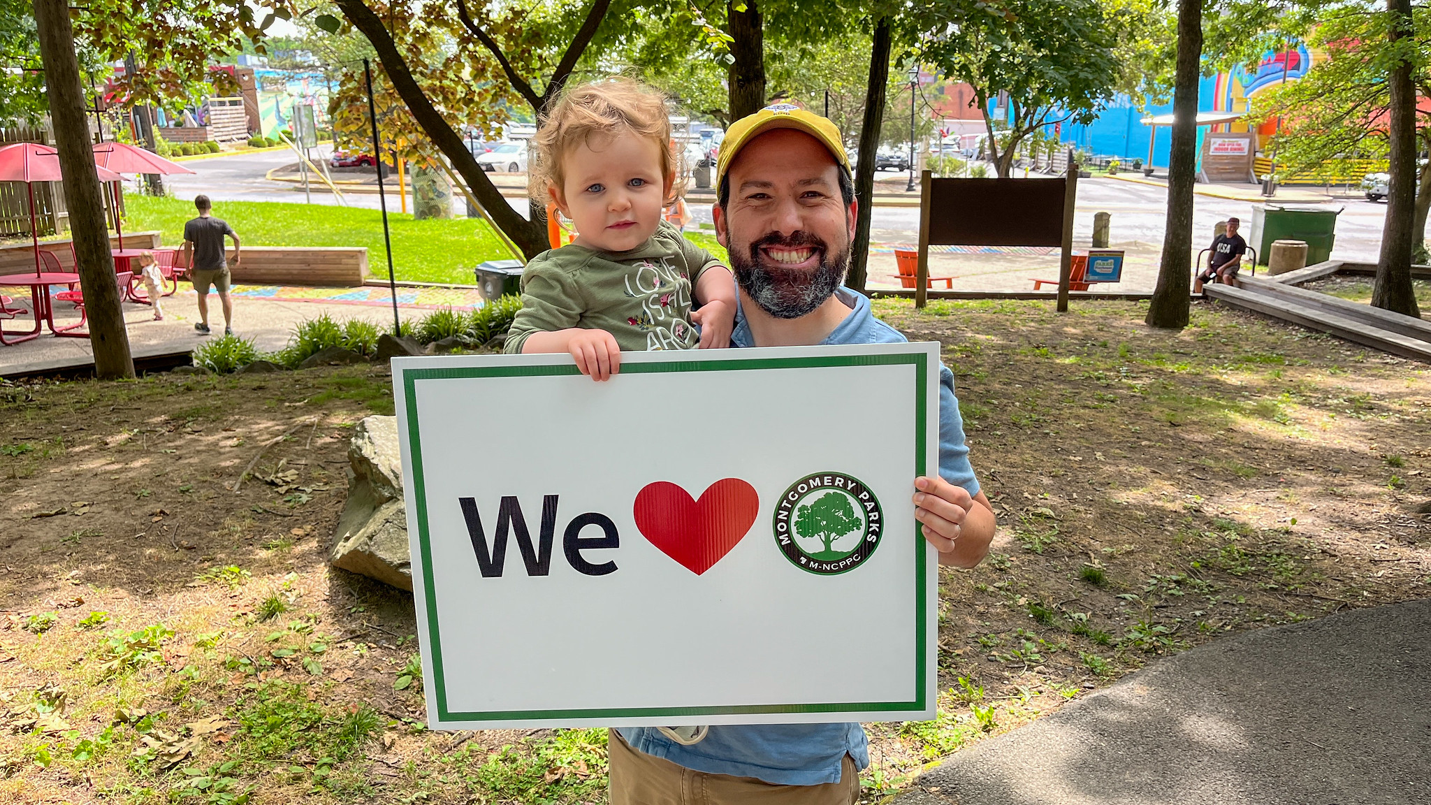 A parent and child holding a "We Love Parks" sign