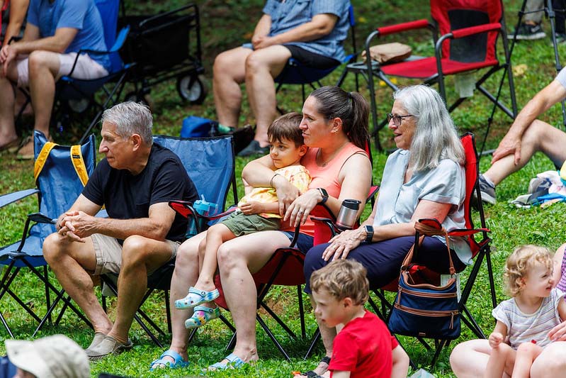 families sitting in camp chairs laughing at the clowns performing at the Happenstance Theater production in summer of 2023