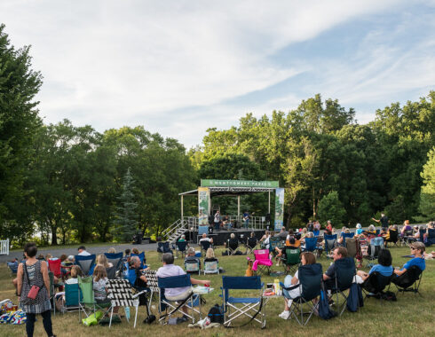 Crowd sitting in lawn chairs and on blankets in front of concert stage