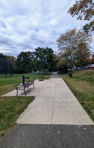 Paved trail with playground, open field, two benches, and water fountain.