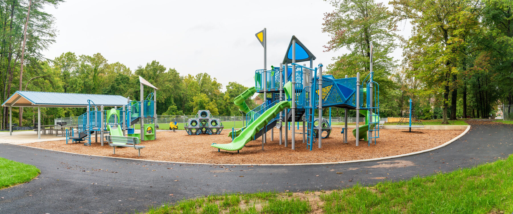 Strathmore Local Park playground with engineer wood fiber surface, bright blue and green structure and a shelter in the background