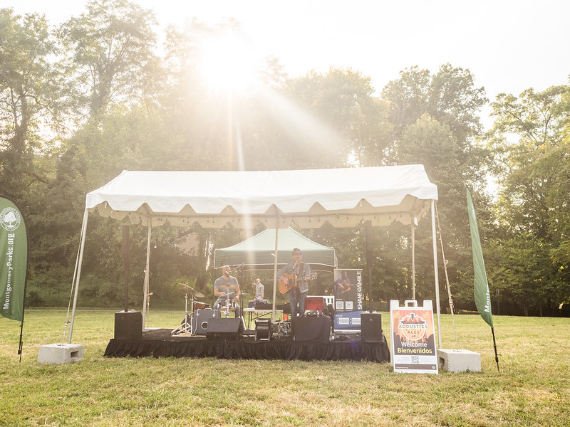 Shame Gamble band performing at Acoustics and Ales September 2024. They play guitar and drums on a stage with tent in grassy field.