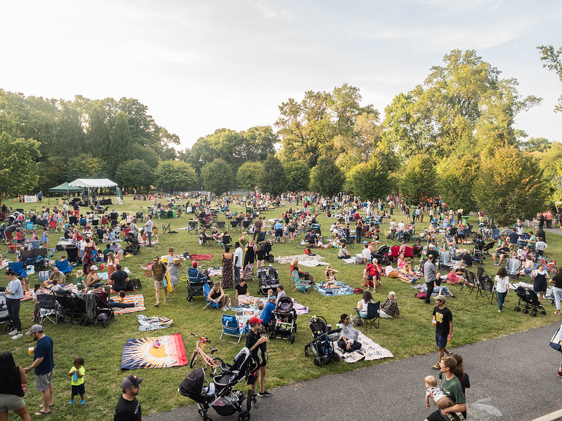 Large grassy field filled with people at the event. Stage is in the background.