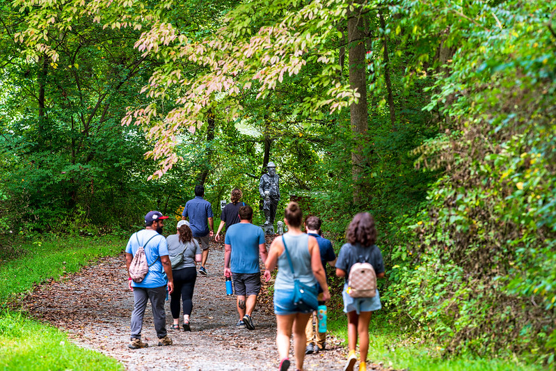 Group of attendees walk trail with living statue in distance