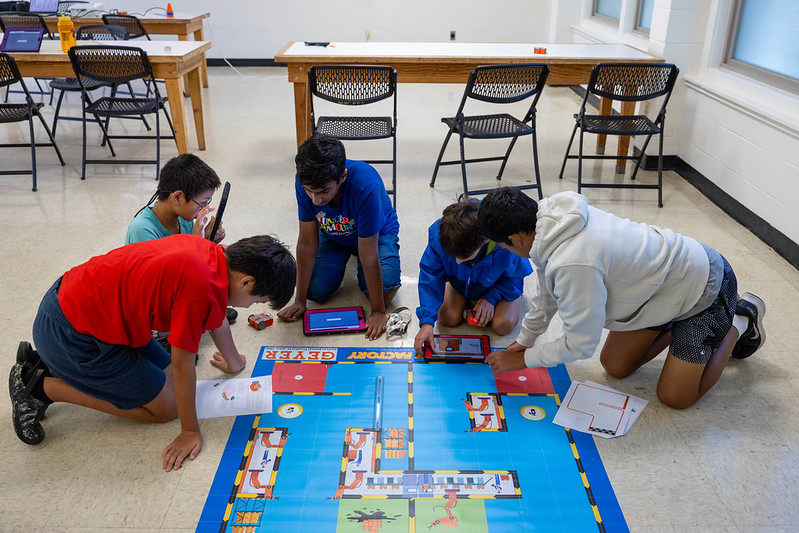 5 kids gather around a blue mat to test out their robots