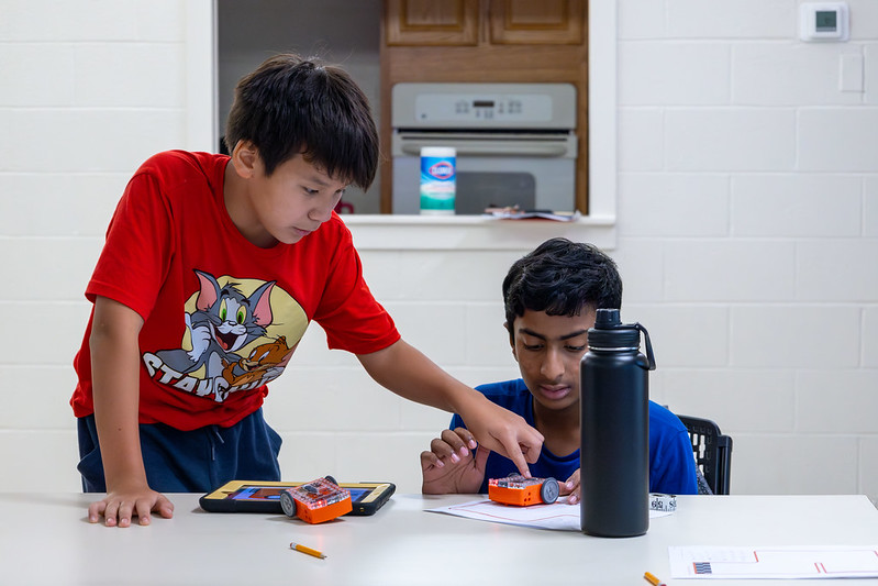 2 boys helping each other. One is touching the others robot.