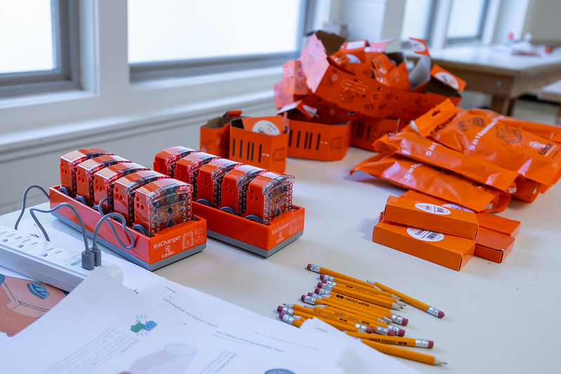 A table full of tools to program robots. There are pencils, kits, and robots charging on the table.