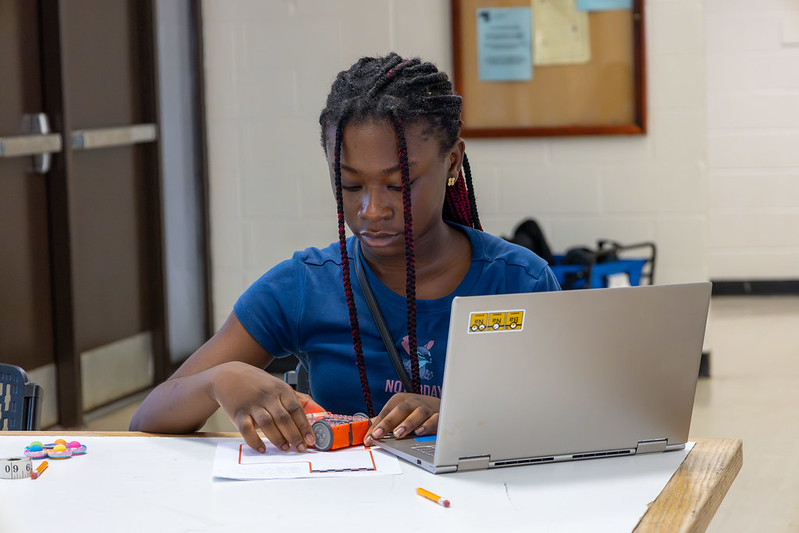 Young girl sits at desk with a laptop, testing her robot out