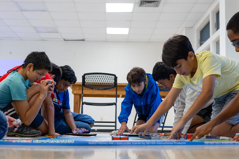 Group of kids testing out robots on a blue mat