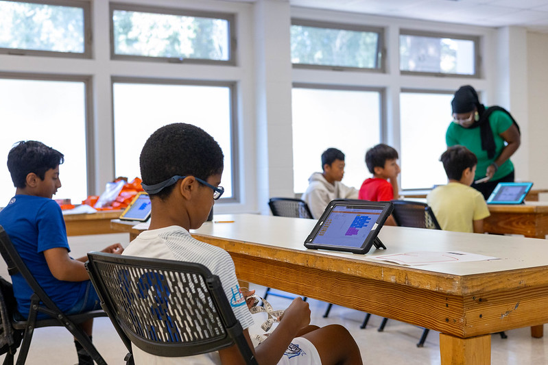 Young attendees use their iPads to program while sitting at tables