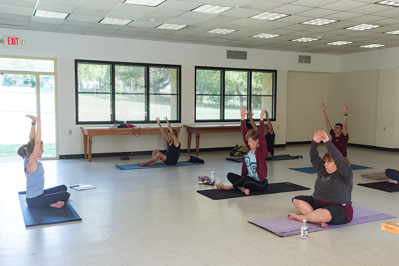 Attendees practice yoga positions, sitting, holding hands above their heads