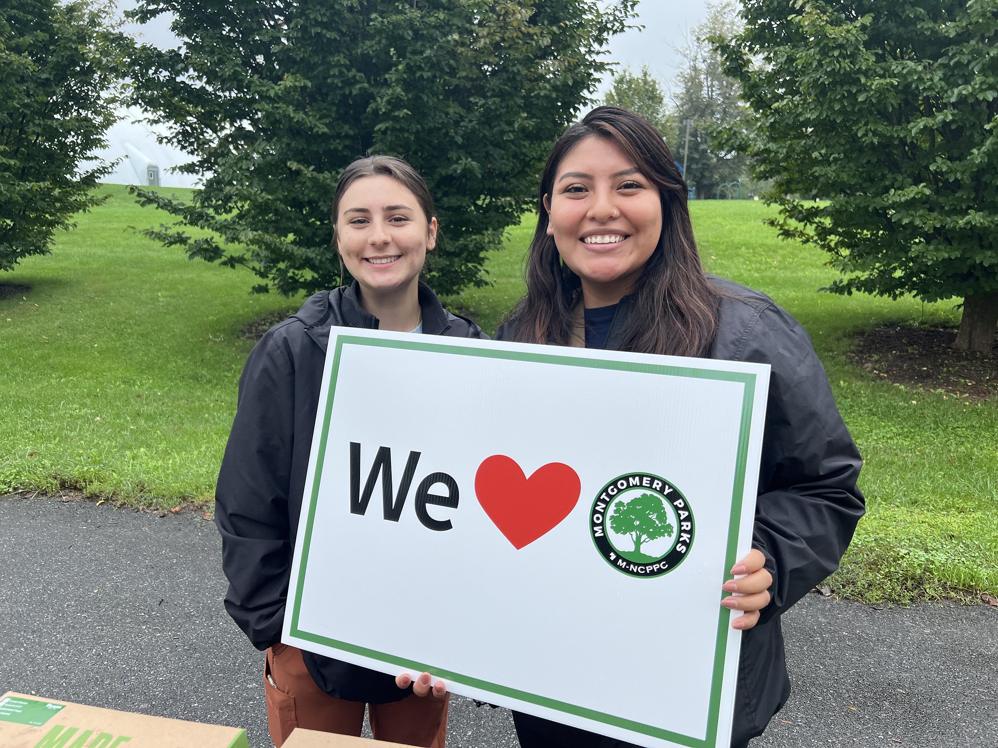 Two people smiling holding a We Heart Parks sign