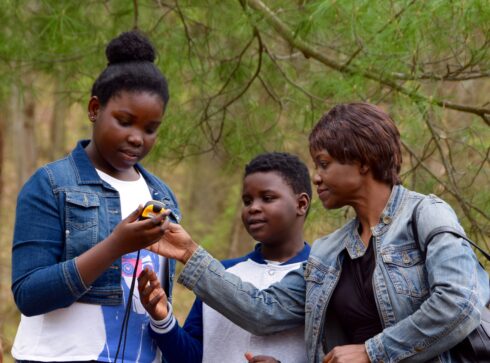 A family of three uses a GPS unit during a geocaching program.