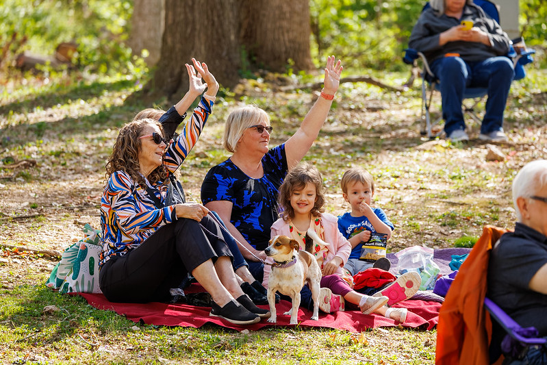 Family sitting on picnic blanket while waving to friends off camera