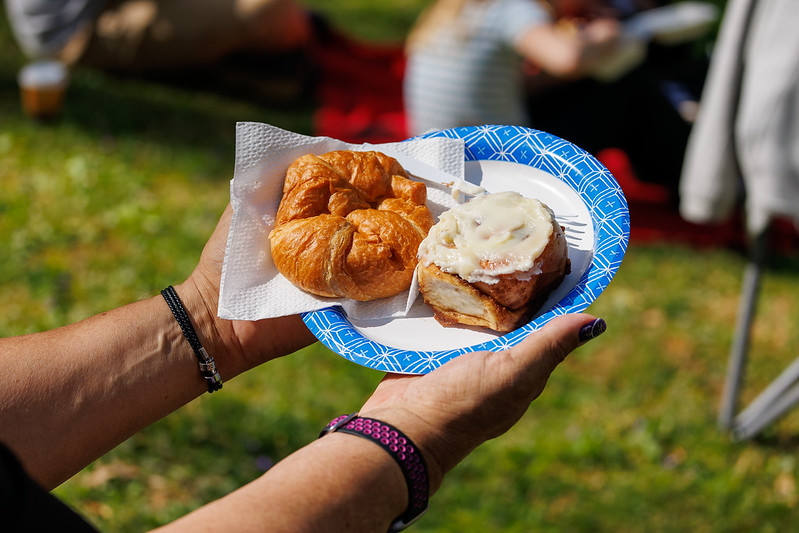 Person holds up plate of cinnamon roll and croissant on a paper plate