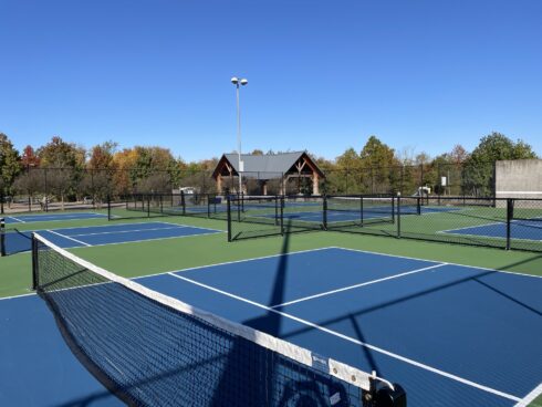 Pickleball courts at East Norbeck Local Park in foreground with trees and pcinic shelter in the background.