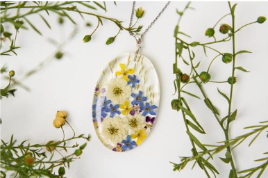 Small bud flowers laying around a resin filled pendant with yellow, white, and blue pressed flowers.