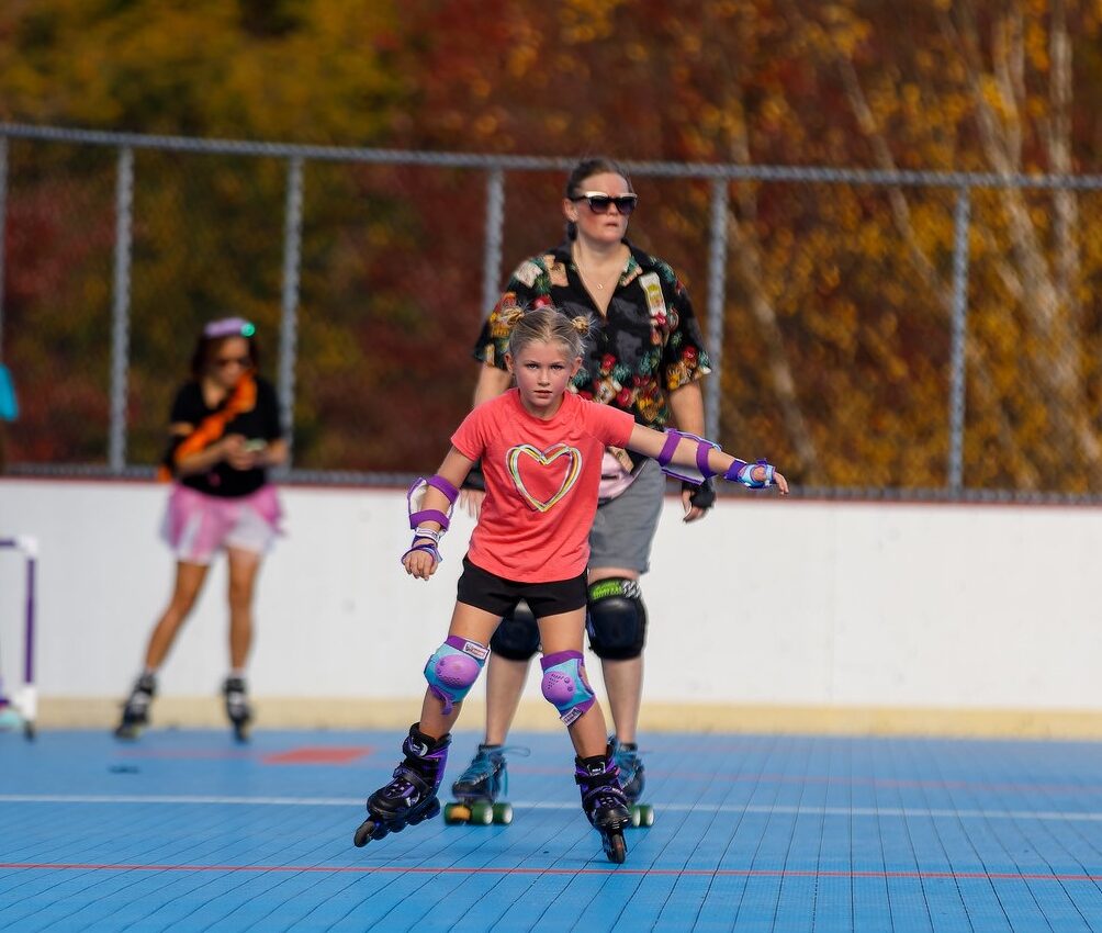 Young girl skates on roller rink with others skate out of focus in the background