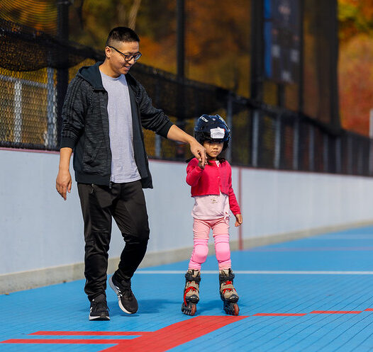 Dad holds young daughter's hand and helps guide her on the roller skate rink