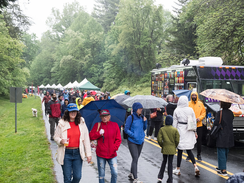 Crowds of people walk on the open parkway with umbrellas in the light rain