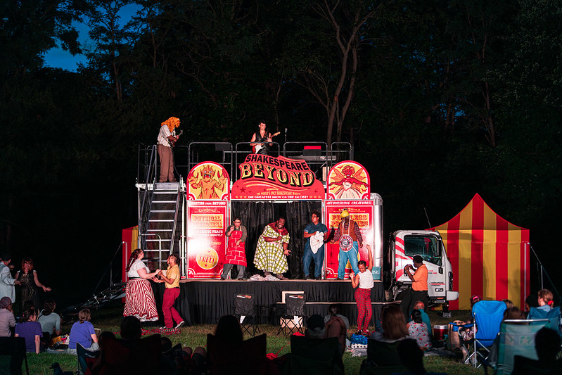 Shakespeare Beyond stage at night lights up while performers sing and dance on the stage and around it