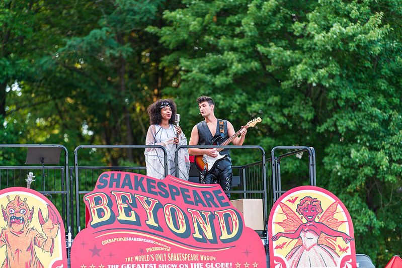 Performers sing into a microphone while one plays guitar