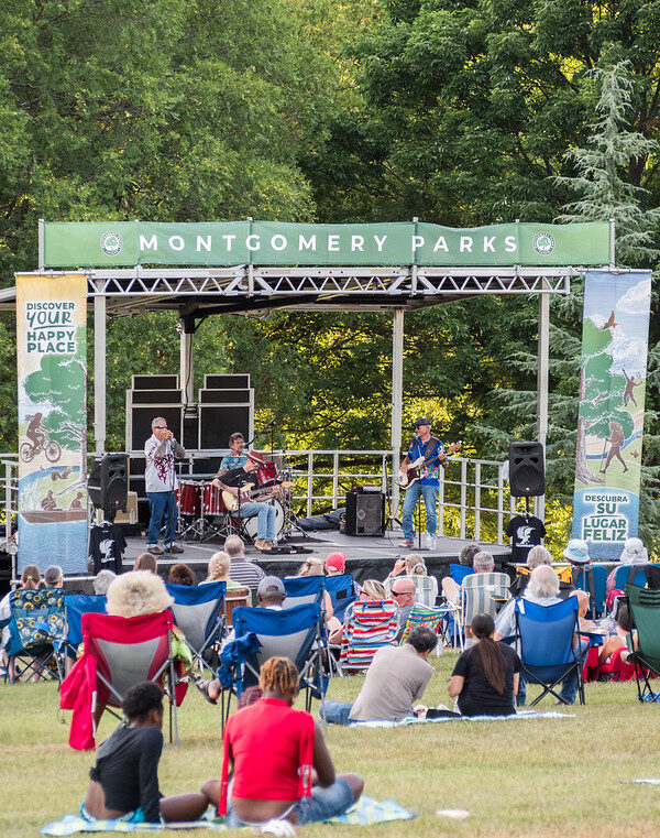 Band plays on stage on the grass while attendees look onward in their chairs