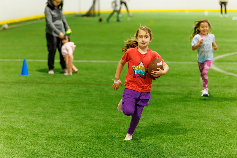 Girl running with a football on the turf field.