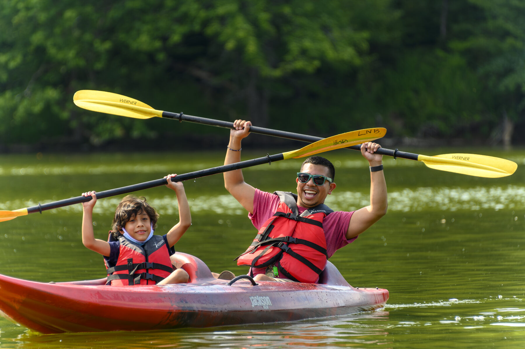 Man and boy in kayak, holding up paddles over heads, at Little Senenca Lake.