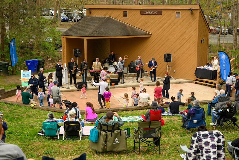 Band of 8 members play on stage as crowd in the lawn watches