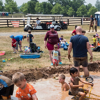 A person driving the ADA Shuttle Cart behind families playing the mud.